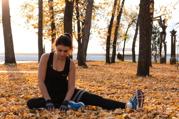 Хабаровск, Россия - 07 октября 2018 года: Юная спортсменка растягивается и готовится к забегу. Привлекательная женщина в спортивной одежде, занимающаяся спортивными упражнениями на природе, на ковре осенних листьев, любит — стоковое фото