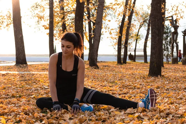 Khabarovsk, Russia - Oct 07, 2018: Young sportswoman stretching and preparing to run. Attractive woman in sports clothes doing sports exercises in nature, on the carpet of autumn leaves, loves — Stock Photo, Image