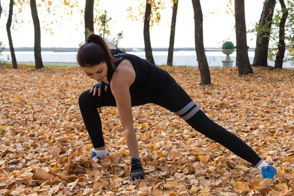 Khabarovsk, Russia - Oct 07, 2018: Young sportswoman stretching and preparing to run. Attractive woman in sports clothes doing sports exercises in nature, on the carpet of autumn leaves, loves gymnast — Stock Photo, Image