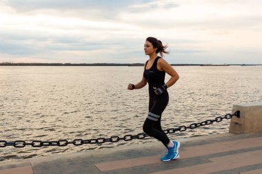 Khabarovsk, Rusya - 07 Ekim 2018: Genç ve çekici bir kız bir şehir Parkı'nda gün batımında koşuyor. Sağlıklı fitness kadın açık havada çalışan. Arka planda Habarovsk ufukta Amur nehri.