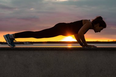 Khabarovsk, Rusya - 07 Ekim 2018: Çekici bir kadın spor elbiseleri günbatımı ve Amur Nehri karşı doğada spor egzersizleri yapıyor jimnastik seviyor, bacaklarını kneads. Aktif genç kız
