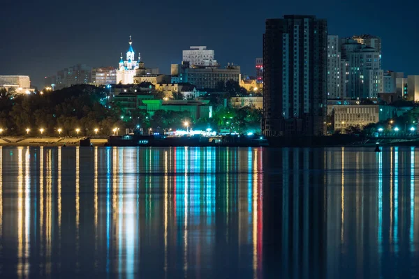 Nachtzicht op de stad Khabarovsk vanaf de rivier de Amur. Blauwe nachtelijke hemel. De nacht stad is fel verlicht met lantaarns. — Stockfoto