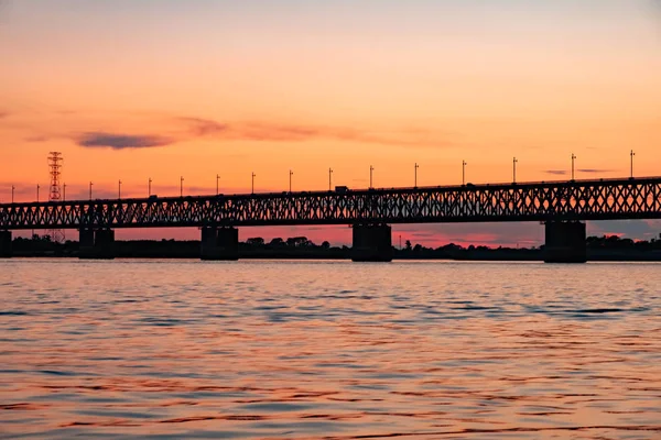 Most nad rzeką Amur o zachodzie słońca. Rosja. Chabarowsk. Zdjęcie z połowy rzeki. — Zdjęcie stockowe