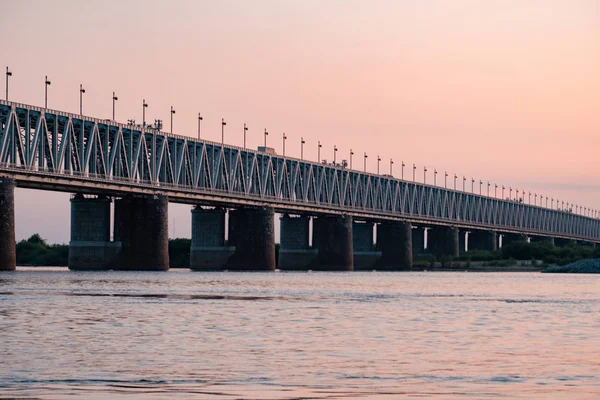 Ponte sobre o rio Amur ao pôr-do-sol. A Rússia. Khabarovsk. Foto do meio do rio . — Fotografia de Stock