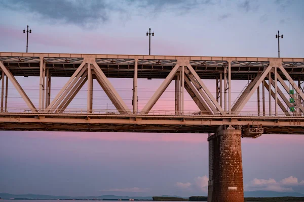 Brug over de Amoer rivier bij zonsondergang. Rusland. Chabarovsk. Foto uit het midden van de rivier. — Stockfoto