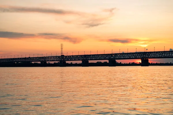 Most nad rzeką Amur o zachodzie słońca. Rosja. Chabarowsk. Zdjęcie z połowy rzeki. — Zdjęcie stockowe