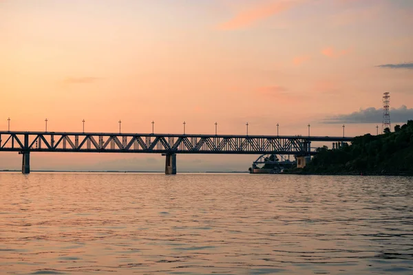 Ponte sobre o rio Amur ao pôr-do-sol. A Rússia. Khabarovsk. Foto do meio do rio . — Fotografia de Stock