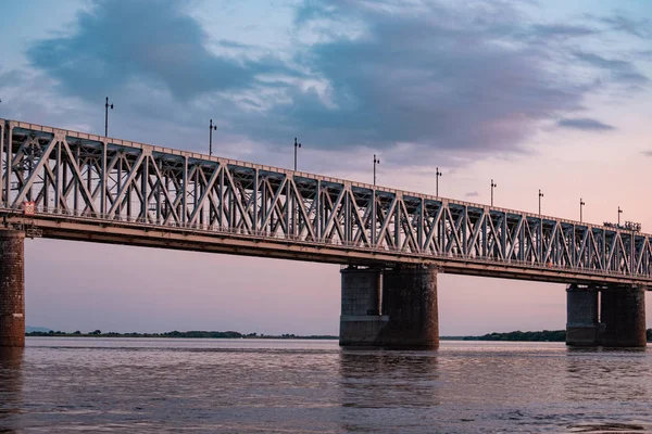 Most nad rzeką Amur o zachodzie słońca. Rosja. Chabarowsk. Zdjęcie z połowy rzeki. — Zdjęcie stockowe