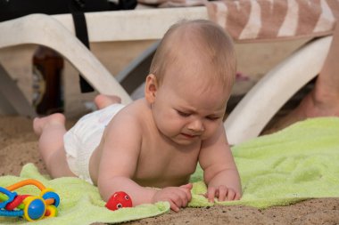 Küçük bir kız kumda uzanıp oyuncaklarla oynuyor..