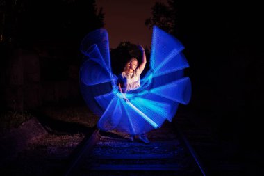 Donmuş ışıkla çevrili genç kız. Işıkla çizim. Uzun pozlama. Sanatsal soyutlama. Dondurucu ışık