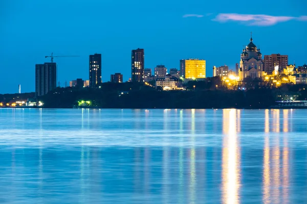 Vista nocturna de la ciudad de Jabárovsk desde el río Amur. Cielo azul nocturno. La ciudad nocturna está brillantemente iluminada con linternas. — Foto de Stock