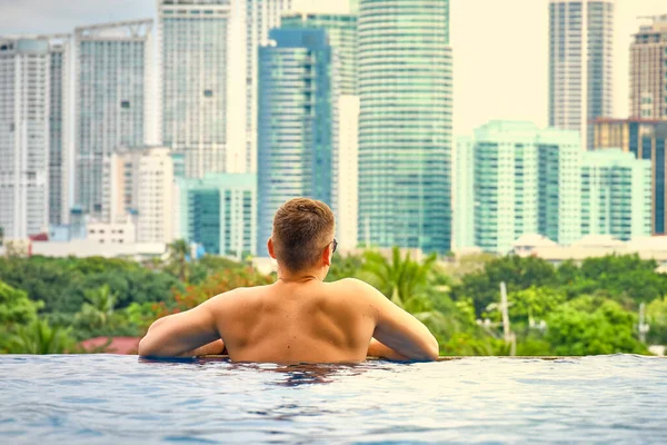 A man in the pool on the roof of the hotel. View of the city of Manila from the pool of the luxury five-star Discovery Primea hotel. Sunny weather. Skyscrapers on the background.