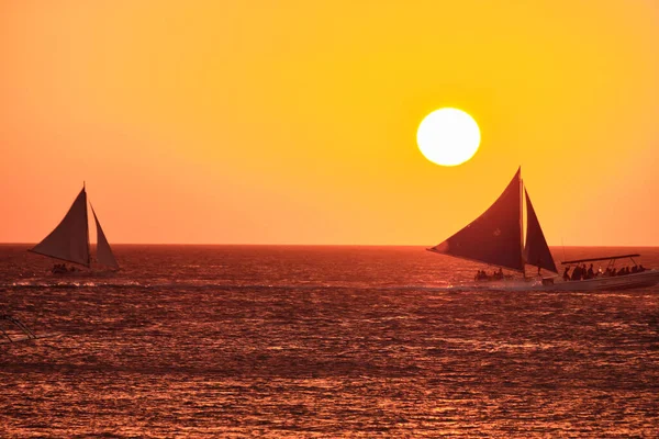 Boracay, Filipinas - 23 de enero de 2020: Puesta de sol en la isla de Boracay. Vela y otros barcos tradicionales con turistas en el mar sobre el fondo del sol poniente. — Foto de Stock