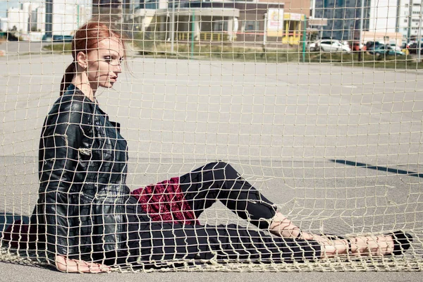 2018 년 9 월 9 일에 확인 함 . Khabarovsk, Russia - Sep 09, 2018: A advanced girl with red hair in a black leather jacket poses in a fashion shot. 바람 이 붉은 스카프를 불고 있어. 볼리볼 넷. — 스톡 사진