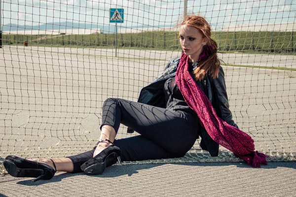 2018 년 9 월 9 일에 확인 함 . Khabarovsk, Russia - Sep 09, 2018: A advanced girl with red hair in a black leather jacket poses in a fashion shot. 바람 이 붉은 스카프를 불고 있어. 볼리볼 넷. — 스톡 사진