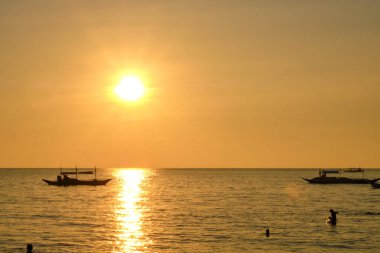 Boracay adasında gün batımı. Yelkencilik ve turistlerle dolu diğer geleneksel tekneler batan güneşin arka planında.