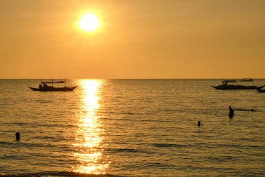 Boracay adasında gün batımı. Yelkencilik ve turistlerle dolu diğer geleneksel tekneler batan güneşin arka planında.