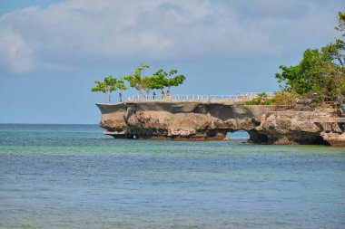 Boracay adasının ünlü simgesi. Denizde küçük bir kaya. Adanın beyaz plajının arka planında turistler fotoğraflanır..