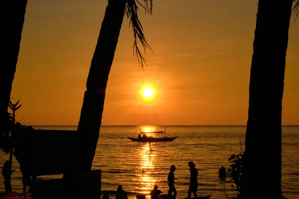 Boracay, Fülöp-szigetek - Jan 27, 2020: Naplemente Boracay szigetén. Vitorlázás és más hagyományos hajók turistákkal a tengeren a háttérben a lenyugvó nap. Turisták ülnek a parton. — Stock Fotó