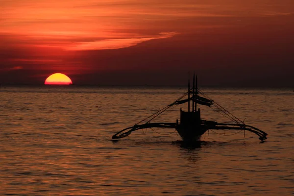 Boracay, Philippinen - 27. Januar 2020: Sonnenuntergang auf der Insel Boracay. Segeln und andere traditionelle Boote mit Touristen auf dem Meer vor dem Hintergrund der untergehenden Sonne. Touristen sitzen am Strand — Stockfoto