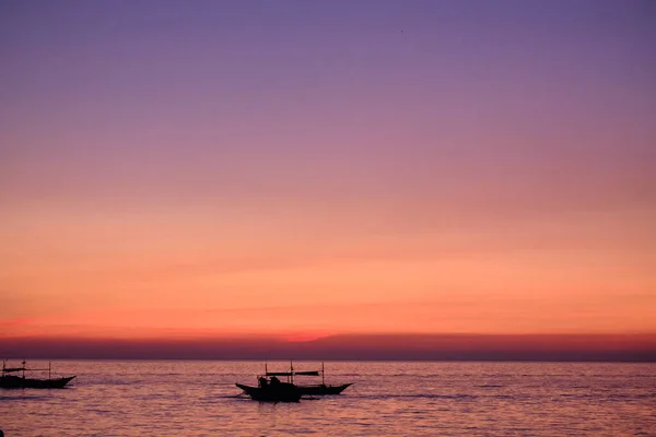 Boracay, Philippinen - 27. Januar 2020: Sonnenuntergang auf der Insel Boracay. Segeln und andere traditionelle Boote mit Touristen auf dem Meer vor dem Hintergrund der untergehenden Sonne. Touristen sitzen am Strand — Stockfoto