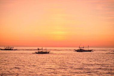 Boracay, Filipinler - 27 Ocak 2020 Boracay Adası 'nda gün batımı. Yelkencilik ve turistlerle dolu diğer geleneksel tekneler batan güneşin arka planına karşı. Turistler sahilde oturuyorlar.