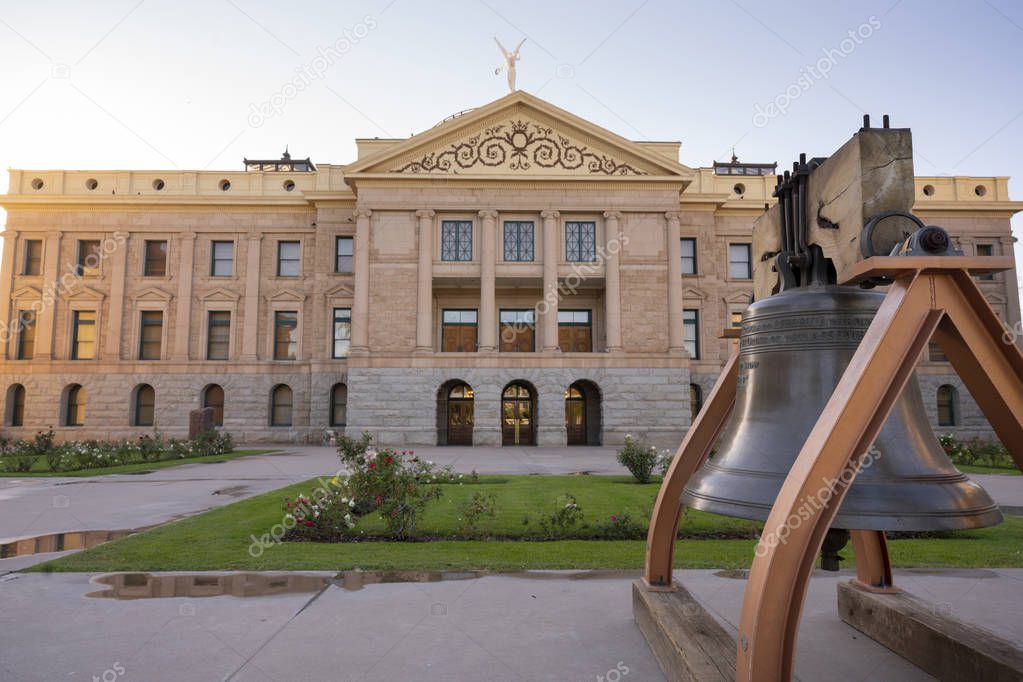 An old watchtower bell is mounted on the sidewalk in front of the state capitol building in Phoenix AZ