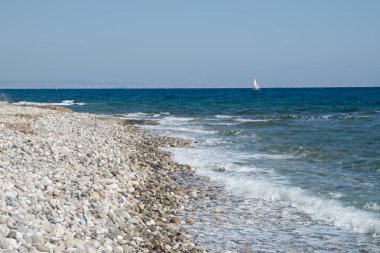Mavi denizde yelken açan küçük beyaz bir yat.