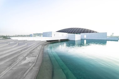 Louvre, Abu Dhabi, United Arab Emirates - Dec.29, 2017: the famous museum of the French architect Jean Nouvel - snow-white boxes under a lace of a dome on turquoise water clipart