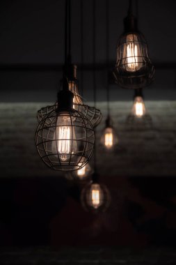 Karanlıkta cam ampuller içinde parlayan filamentler ile endüstriyel tarzı tel lambalar. Parlak ışıklar ve koyu arka plan. Tel kafes abajurları ile Kentsel tarzı iç aydınlatma. Grunge dekorasyonu. Eski moda iç dekorasyon. Açık ve karanlık