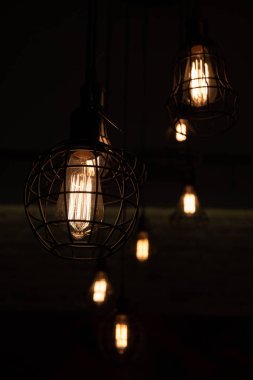 Metal tel abajurlar tavandan asılı. Büyük cam ampuller içinde parlayan filament ile Lambalar. Geometrik çizgiler ve çeşitli karkas şekiller. Kentsel tarzı iç aydınlatma. Tel avize yakın çekim. Geometrik tel karkas avizeler.