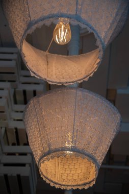 Vintage tekstil abajur ve cam ampul içinde parlayan filament ile Rustik tarzı avize. Arka arkaya iki eski şık tavan lambası. Süslü dantel örgü ile süslenmiş retro lambalar. Eski moda iç nesneler. Ev dekorasyonu öğeleri. Rustik stil 