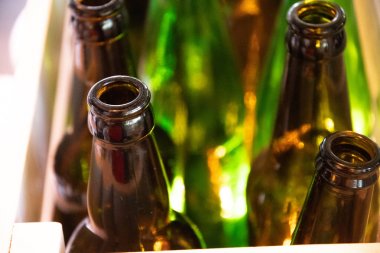 Boş şişe cam darboğazları yakın çekim. Retro şekilli bira şişeleri Cilalı temiz cam doku. Arka plan olarak arka plan olarak arka ışık ve bulanık yeşil şişeler ile şeffaf kahverengi cam parlayan yüzey. Cam doku yakın çekim. Şişelerin depolama konsepti