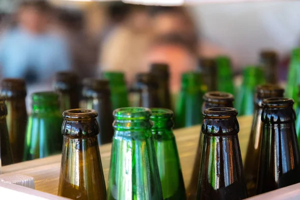 Bottle tops of open glass bottles with blurred background. Glowing clear glass bottlenecks. Green and brown glass beer bottles in a rows. Shiny glass reflective surface closeup. Beer party concept. Glass texture closeup. Storage concept of bottles