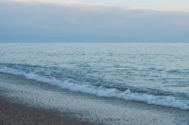 Mavi dumanlı gökyüzü ile mor alacakaranlık akşam gün batımı sakin deniz sörfü. Karadeniz kıyılarının deniz manzarası. Sallanan deniz gelgitıslak plaj kum geliyor. Çapraz kıyı şeridi. Seyahat manzarası. Deniz kenarında sakin manzara 