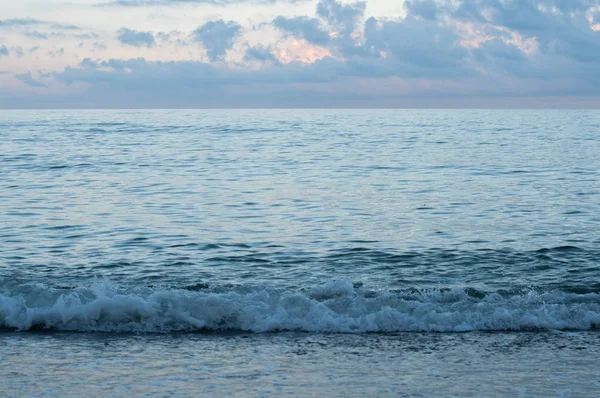 夏日黄昏的海岸线在蓝色日落的傍晚与美丽的丁香云在天空 黑海海岸的海景 摇曳的大海来到潮湿的沙滩沙 旅游风景 宁静的海景 — 图库照片
