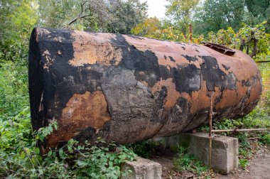 Paslı metal yüzeyde berbat siyah boya lekeleri ile kaplı eski harap su tankı. Sofiyivsky parkta yeşil açık yerde eski Vintage varil 