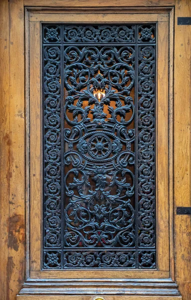 Çerçeveli kapı paneli ile vintage ahşap kapı kaprisli süslü ızgaralar. Arka ışık ile antika süslü metal kafes closeup. Paris Fransa'da antika kapı. Barok mimari detaylar.
