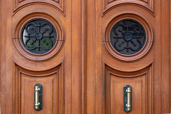 Çerçeveli kapı panelleri ve süslü metal kafesler tarafından korunan yuvarlak pencereler ile Vintage ahşap kapı. Paris Fransa'da antikçift kapı yaşlı ahşap yüzeyinde parlak pirinç kapı kolları. Simetri şekilleri.
