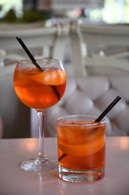 Şarap kadehi ve cam parlak turuncu Aperol Spritz kokteyl beyaz iç bulanık arka plan üzerinde siyah içme pipetleri ile. Taze portakal dilimleri ile iki soğuk kokteyl. Yaz alkollü içecekler.