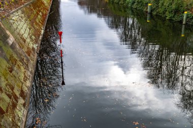 Berlin Almanya'da Spree nehri pürüzsüz yansıtıcı su yüzeyi. Eski taş duvar seti. Yüzen sonbahar yaprakları ile karanlık suda çıplak ağaçların ve bulutlu gökyüzünün bulanık yansıması. Sonbahar görünümü.