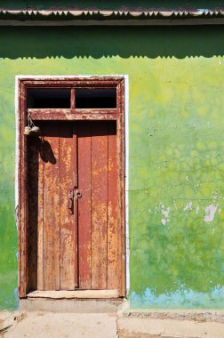 Desenli çatı ile geleneksel çiftlik binası yeşil kırık alçı cephe eski kırmızı sıkıntılı ahşap kapı. Ukrayna kırsalında terk edilmiş evin kapalı kapı ve kaba çizik duvarlar.  