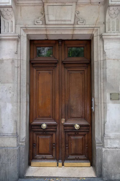 Dark wood double door entrance of old building in Paris France. Antique wooden doorway with golden metal doorknobs and stone wall of classic architecture house with relief architectural details.