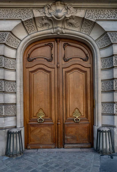 Gorgeous style arch with double door entrance of old building in Paris France. Vintage wood doorway and fretwork wall of ancient house with sculptural volute above door. Ornate door knockers. Architecture of Paris France. Antique building exterior.