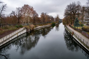 Berlin Almanya'da bulutlu gökyüzü altında sakin su ve çıplak ağaçlar ile Nehir manzara. Nehir su yüzeyinde karanlık yansıma. Sonbahar havası. Nehir kıyılarına perspektif görünümü.