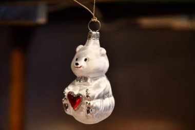 Kırmızı kalp ve gümüş glitter detayları ile küçük beyaz bebek ayı şeklinde Sevimli cam Noel süsü. Noel adil hikaye özniteliği karanlık arka plan üzerinde closeup. Yeni Yıl dekorasyonu.