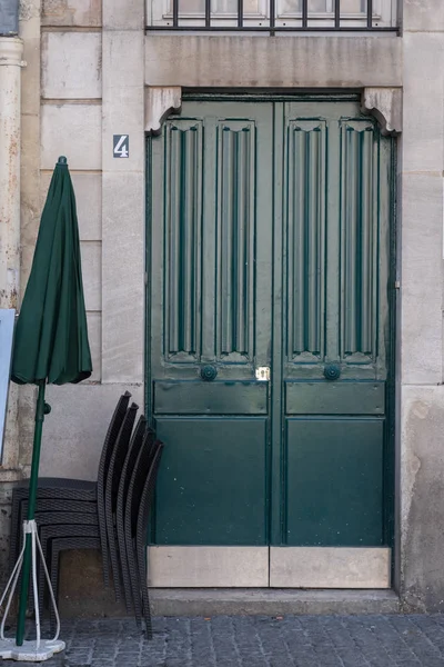 Minimal style wooden door painted in deep green color and closed green parasol nearby. Elegant classical style entrance of retro building in Paris France. Front door of house.