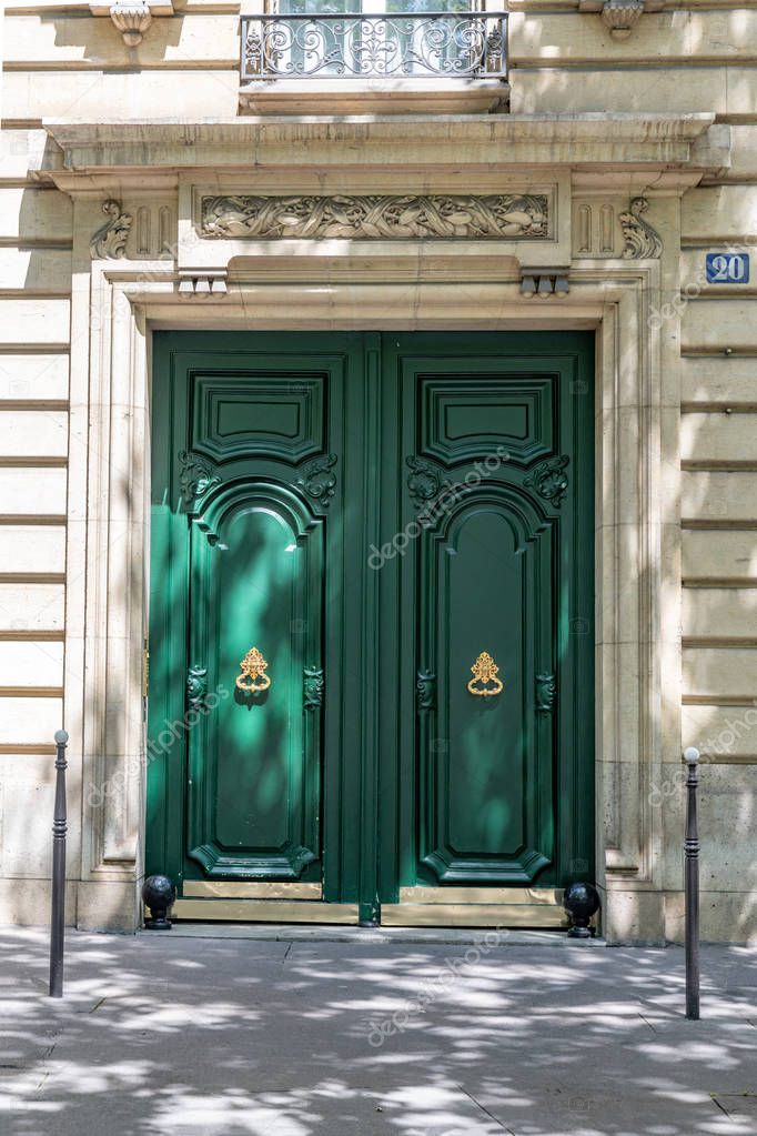 Entrance with double door painted in bright green color. Elegant doorway of white stone building in Paris France. Green wooden door panels with ornate golden metal door knockers. Shadows from foliage.