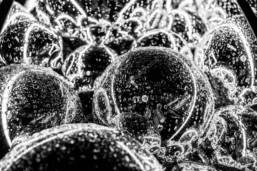 Shiny mirror glass bulbs with drops of rain in night light. Sparkling glares reflected in silver ball surface. Christmas ornament closeup. Christmas lights. Holiday decor. New Year decorations. Black and white photo. Monochrome abstraction background