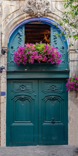 Beautiful ornate turquoise green door with purple flowers on window above. Baroque architecture of Paris France. Antique building exterior fretwork entrance and stone wall with sculptural details.